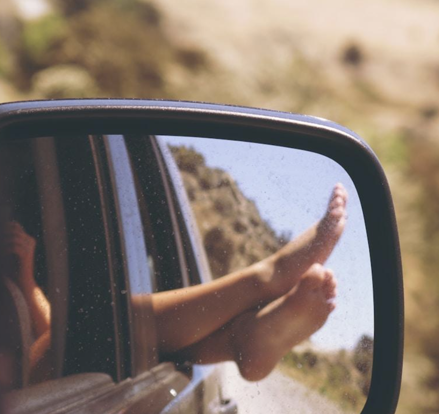 Bare feet reflected in a car's side mirror.